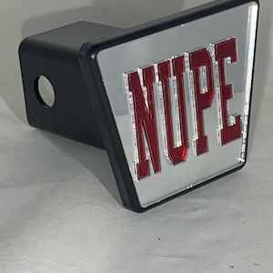 May include: A black hitch cover with a silver reflective surface and the word "NUPE" in red lettering.