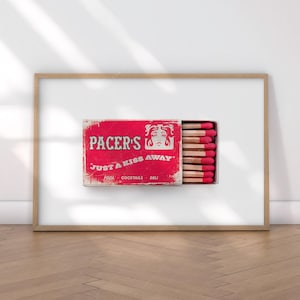 K&ouml;nnte beinhalten: Gerahmter Druck mit einer roten Vintage-Streichholzschachtel mit dem Text "PACER'S JUST A KISS AWAY". Die Schachtel ist ge&ouml;ffnet und zeigt Streichh&ouml;lzer mit roten K&ouml;pfen. Der Hintergrund ist wei&szlig;.