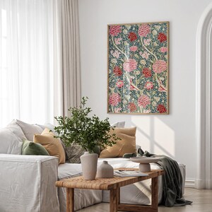 May include: A white sofa with green and beige cushions, a green throw blanket, and a wooden coffee table. A potted plant sits on the table, and a framed floral print hangs on the wall behind the sofa.