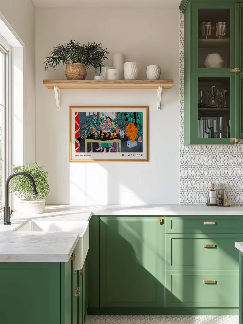 May include: A framed Henri Matisse art print featuring a colorful interior scene with a person at a table, displayed on a white wall above green kitchen cabinets, a white farmhouse sink, and a wooden shelf holding various white ceramic vases.