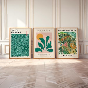 May include: Three framed wall art prints. The left print features Yayoi Kusama text over a green field of circles. The center print shows Matisse text, a yellow sun, and green leaves on a pink background. The right print displays Flower Market New York text over a detailed botanical illustration.