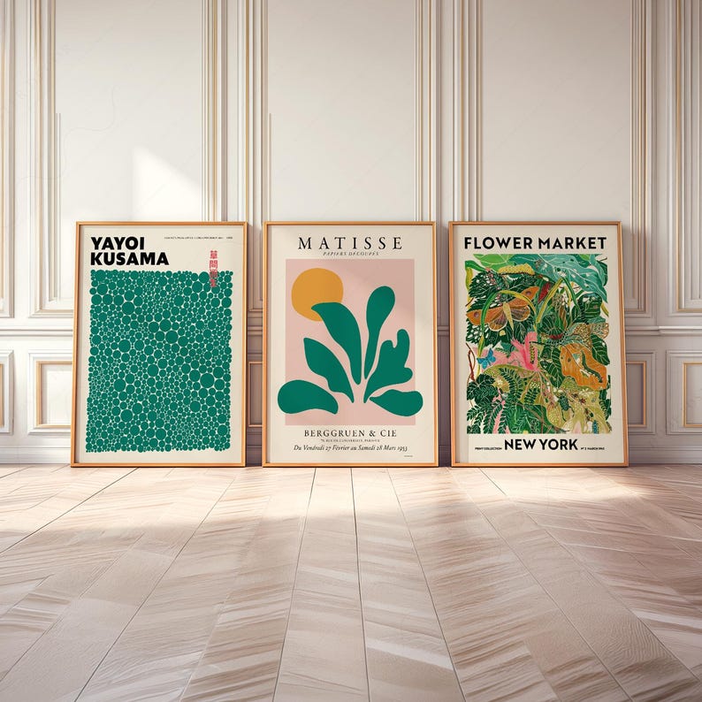 May include: Three framed wall art prints. The left print features Yayoi Kusama text over a green field of circles. The center print shows Matisse text, a yellow sun, and green leaves on a pink background. The right print displays Flower Market New York text over a detailed botanical illustration.