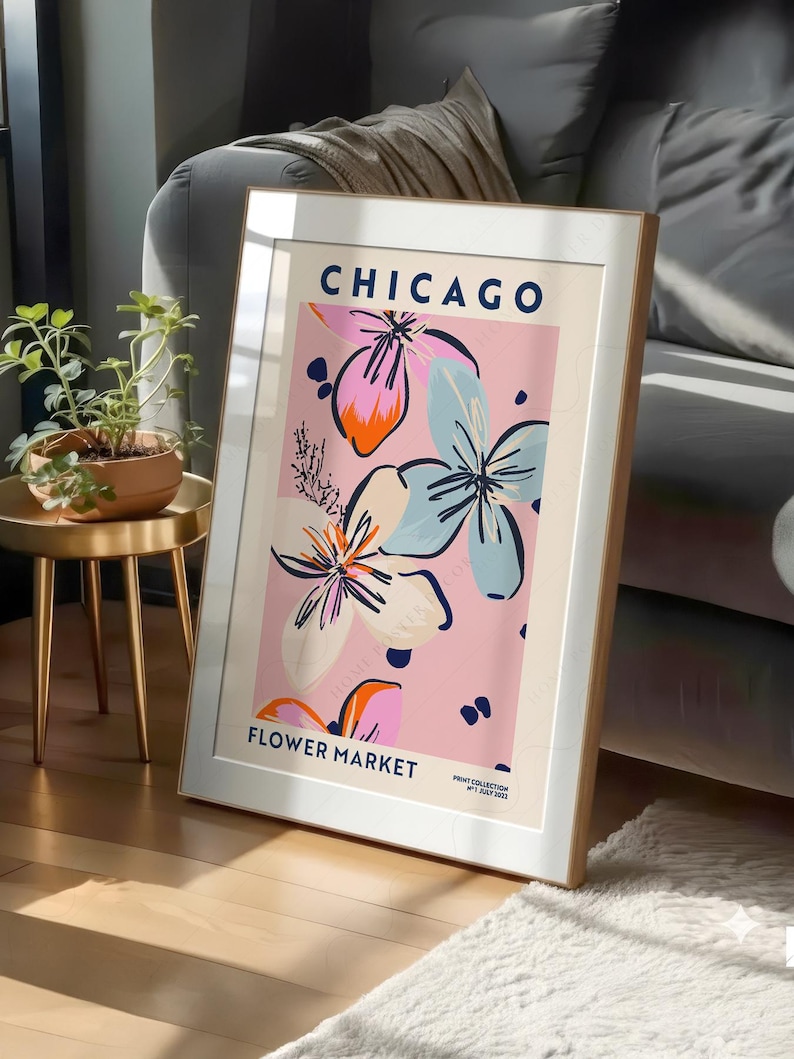 May include: A framed vertical art print featuring the text CHICAGO FLOWER MARKET in dark blue. The design displays stylized floral illustrations in shades of pink, light blue, and orange against a pale pink background with dark blue accents.