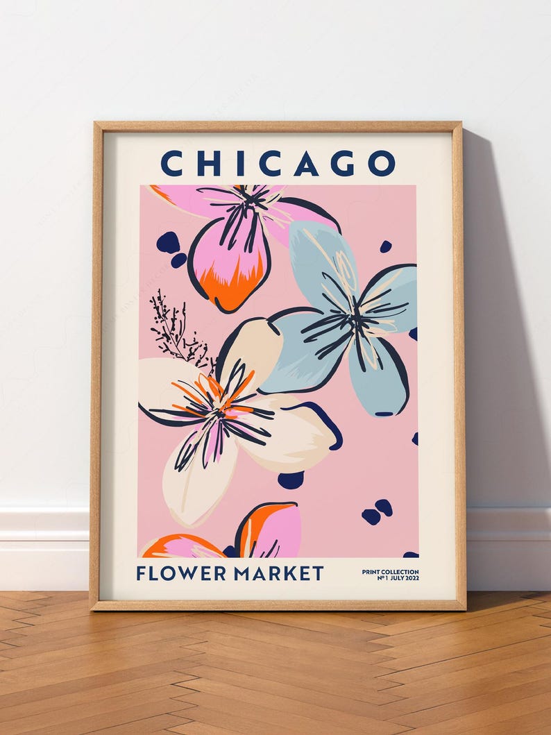 May include: A framed wall art print featuring the text CHICAGO FLOWER MARKET PRINT COLLECTION N&deg;1 JULY 2022. The design displays stylized floral illustrations in shades of pink, light blue, and orange against a soft pink background.