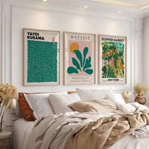 May include: Three framed wall art prints hanging above a bed. The left print features green dots by Yayoi Kusama. The center print shows a yellow circle and green leaves by Matisse. The right print displays a colorful floral flower market design.
