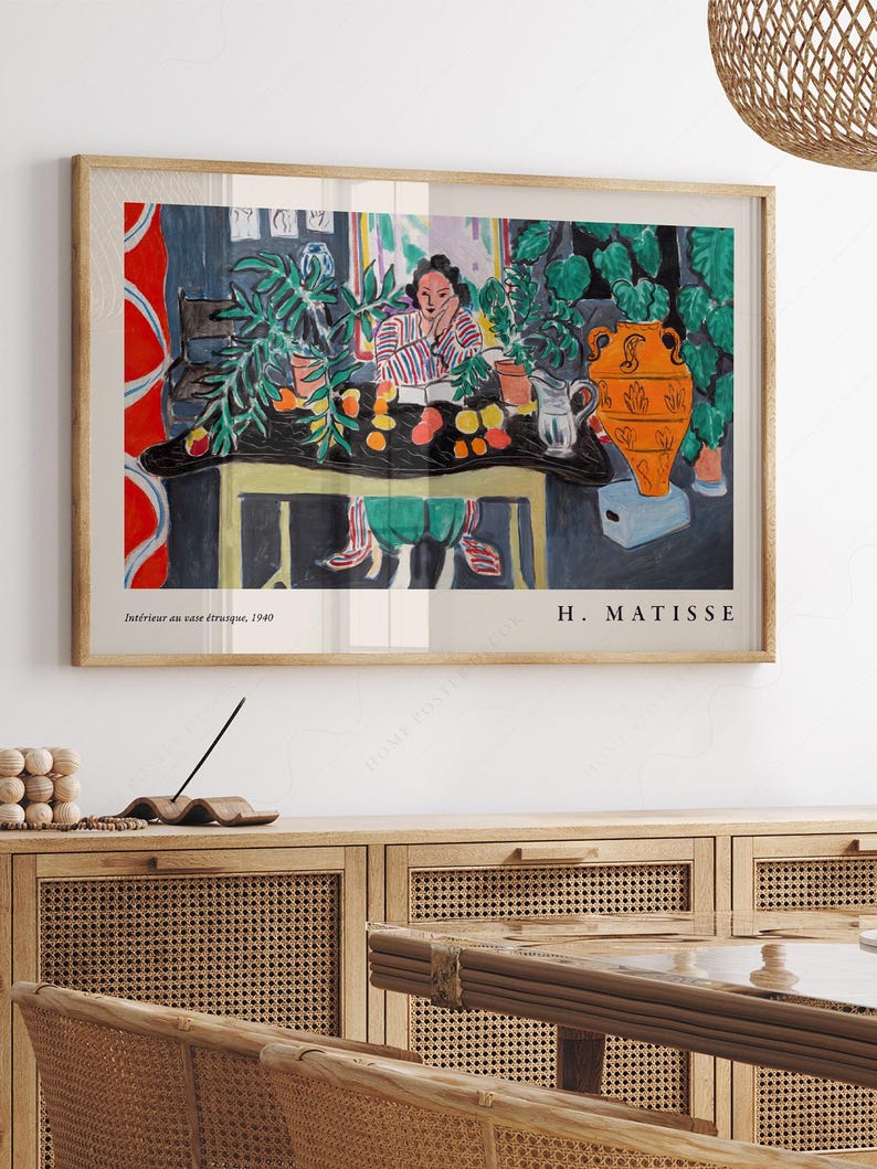 May include: A framed art print of Henri Matisse's 1940 painting Int&eacute;rieur au vase &eacute;trusque. The artwork depicts a person sitting at a table with plants, fruit, and a large orange vase. The print includes the text Int&eacute;rieur au vase &eacute;trusque, 1940 and H. MATISSE.