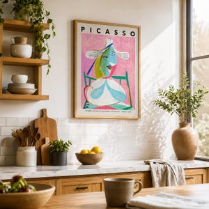 May include: A framed art print of Pablo Picasso's Femme Assise au Chapeau de Paille, featuring a stylized portrait in pink, blue, and green tones. The print includes the text PICASSO at the top and the title at the bottom, displayed on a wall.