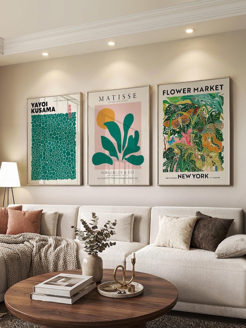 May include: Three rectangular wall art prints in light wood frames. The left print features green dots and the text YAYOI KUSAMA. The center print shows green leaves, a yellow circle, and the text MATISSE BERGGRUEN & CIE. The right print displays botanical illustrations and the text FLOWER MARKET NEW YORK.
