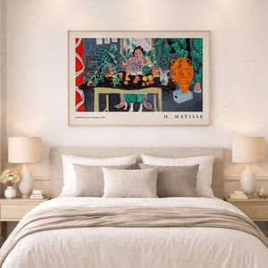 May include: A framed art print of Henri Matisse's painting titled Int&eacute;rieur aux aubergines, 1948. The artwork depicts a person sitting at a table with a black cloth, green plants, an orange vase, and fruit, with the text H. MATISSE at the bottom.