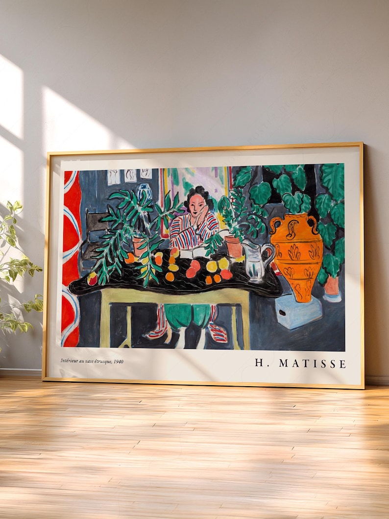 May include: A framed art print of Henri Matisse's painting Int&eacute;rieur au vase &eacute;trusque, 1940. The artwork depicts a person sitting at a table with a large orange vase, green plants, and fruit, rendered in a colorful, expressive style with bold lines.