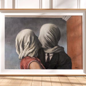 May include: A framed art print depicting two figures with their heads covered in white fabric. One figure wears a red top, while the other wears a dark suit and tie. The background features a grey wall and a vertical orange panel, all encased in a light wood frame.