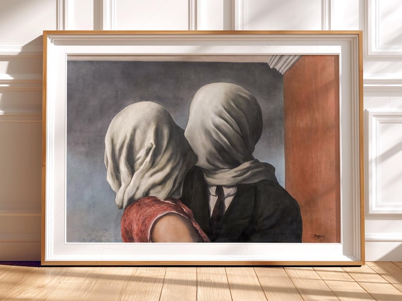 May include: A framed art print depicting two figures with their heads covered in white fabric. One figure wears a red top, while the other wears a dark suit and tie. The background features a grey wall and a vertical orange panel, all encased in a light wood frame.