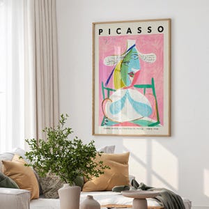 May include: A framed art print titled PICASSO featuring a stylized portrait of a figure in a straw hat. The artwork uses a vibrant palette of pink, green, blue, and yellow. The text at the bottom reads FEMME ASSISE AU CHAPEAU DE PAILLE - PARIS 1938.