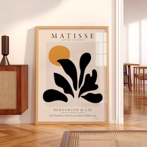 May include: A framed Matisse Papiers D&eacute;coup&eacute;s exhibition poster featuring a yellow circle and black organic shapes on a light background. The text reads MATISSE PAPIERS D&Eacute;COUP&Eacute;S, BERGGRUEN & CIE, 70, RUE DE L'UNIVERSIT&Eacute;, PARIS-VII, Du Vendredi 27 F&eacute;vrier au Samedi 28 Mars 1953.