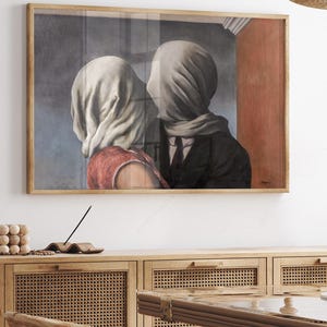 May include: A framed rectangular wall art print depicting two figures with their heads covered in white fabric. The figure on the left wears a red garment, while the figure on the right wears a dark suit and tie. The background features a blue wall.