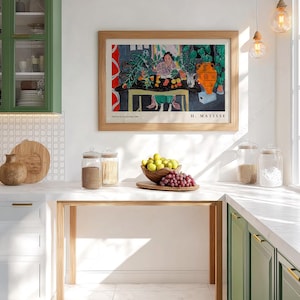 May include: A framed art print of Henri Matisse's 'Int&eacute;rieur aux aubergines' featuring a colorful still life with a person, plants, and an orange vase, displayed on a white wall above a kitchen counter with glass jars and a bowl of fruit.