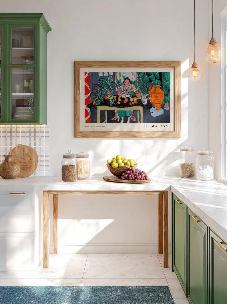 May include: A framed art print of Henri Matisse's 'Int&eacute;rieur aux aubergines' featuring a colorful still life with a person, plants, and an orange vase, displayed on a white wall above a kitchen counter with glass jars and a bowl of fruit.