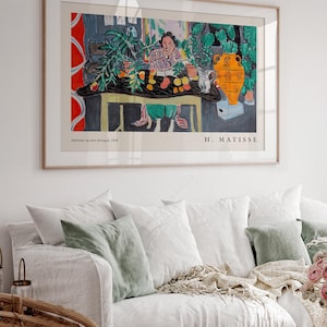 May include: A framed art print of Henri Matisse's Int&eacute;rieur aux aubergines, 1940. The painting depicts a person sitting at a table with a black cloth, green plants, a yellow vase, and fruit. The text reads Int&eacute;rieur aux aubergines, 1940 and H. MATISSE.