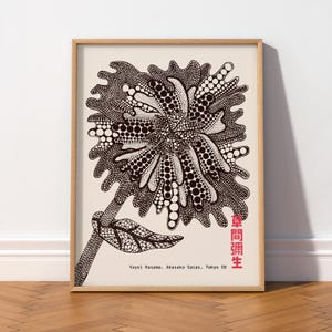 May include: A framed art print featuring a black and white graphic illustration of a stylised flower covered in polka dots. The text "Yayoi Kusama, Akasaka Sacas, Tokyo 08" is printed in black, with the artist's name in red Japanese characters.