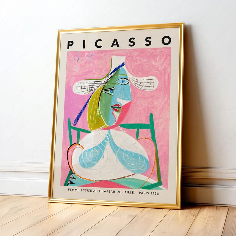 May include: A framed art print featuring Pablo Picasso's painting titled Femme Assise au Chapeau de Paille, Paris 1938. The artwork displays a stylized figure in a straw hat against a pink background, set within a thin, metallic gold frame.