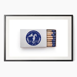 K&ouml;nnte beinhalten: Eine rechteckige Streichholzschachtel mit einem blau-wei&szlig;en kreisf&ouml;rmigen Logo mit der Aufschrift "The Beach Club 1928" und einem Seepferdchen und einer Flagge. Die Schachtel ist ge&ouml;ffnet und zeigt Streichh&ouml;lzer mit blauen Spitzen.