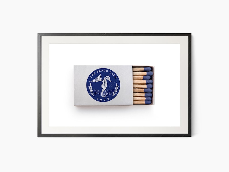 K&ouml;nnte beinhalten: Eine rechteckige Streichholzschachtel mit einem blau-wei&szlig;en kreisf&ouml;rmigen Logo mit der Aufschrift "The Beach Club 1928" und einem Seepferdchen und einer Flagge. Die Schachtel ist ge&ouml;ffnet und zeigt Streichh&ouml;lzer mit blauen Spitzen.