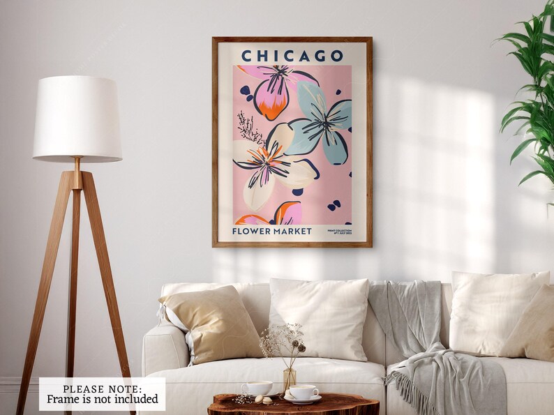 May include: A rectangular wall art print featuring the text CHICAGO FLOWER MARKET in dark blue. The design displays stylized floral illustrations in shades of pink, light blue, and orange against a soft pink background, presented in a wooden frame.