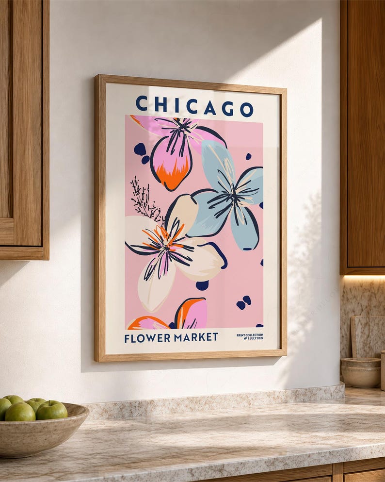 May include: A framed wall art print featuring the text CHICAGO FLOWER MARKET and PRINT COLLECTION N&deg;1 JULY 2022. The graphic design displays stylized flowers in shades of pink, light blue, orange, and dark blue against a soft pink background.