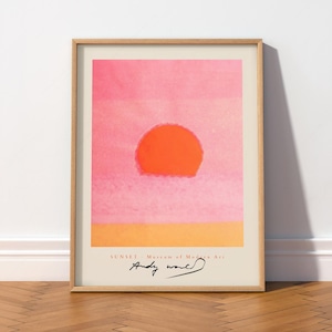 May include: A framed art print featuring a stylised orange sun against a pink gradient background and a yellow horizon line. The text reads SUNSET - Museum of Modern Art with the signature Andy Warhol printed in black ink at the bottom centre.