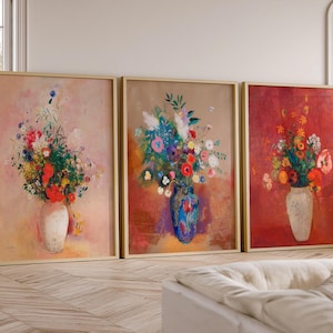 May include: Three framed floral paintings. Each depicts a vase filled with colourful flowers. The paintings have a warm colour palette with shades of red, pink, and brown. The frames are a light wood colour.