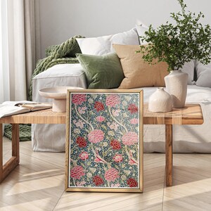 May include: A framed print of a floral pattern with pink and red flowers on a dark blue background. The print is sitting on a wooden table in a living room setting.