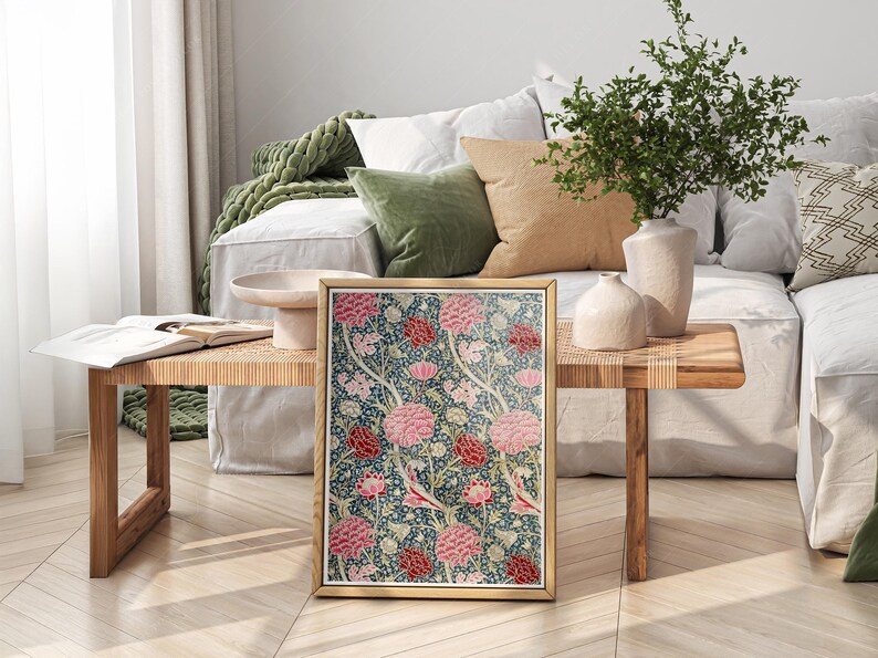 May include: A framed print of a floral pattern with pink and red flowers on a dark blue background. The print is sitting on a wooden table in a living room setting.