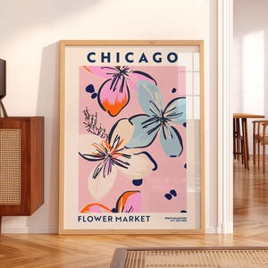 May include: A framed wall art print titled CHICAGO FLOWER MARKET PRINT COLLECTION N&deg;1 JULY 2022. The poster features a light pink background with stylized floral illustrations in shades of blue, orange, cream, and dark pink with black outlines.