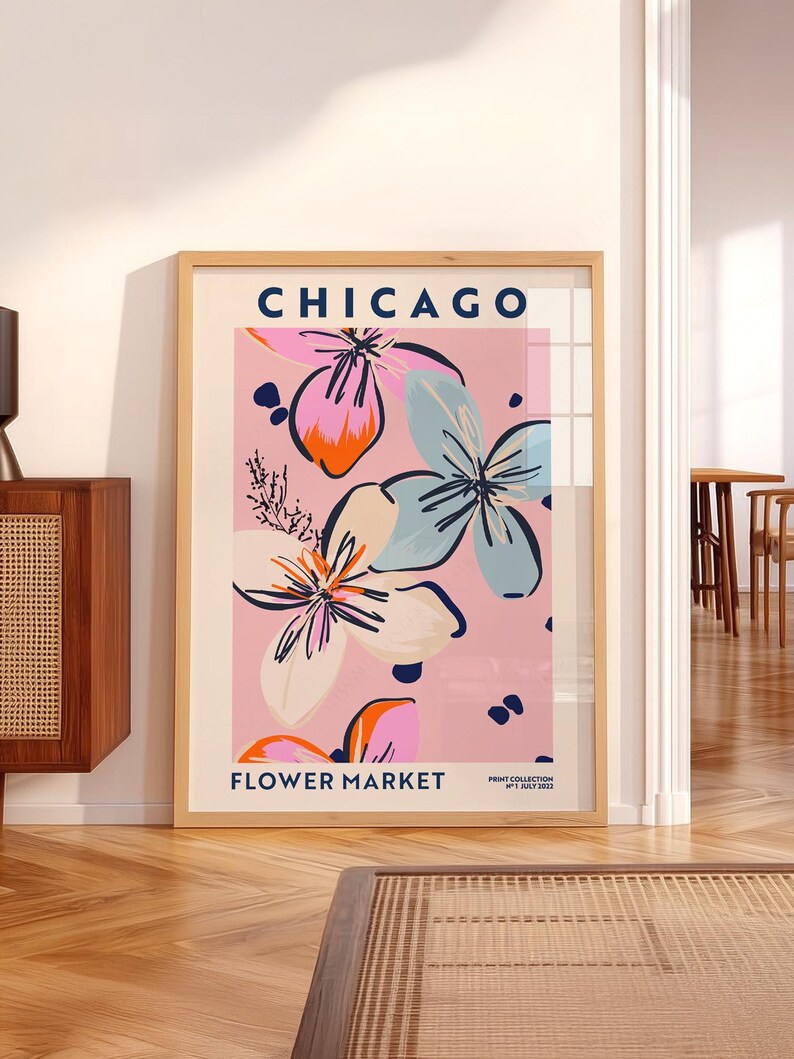 May include: A framed wall art print titled CHICAGO FLOWER MARKET PRINT COLLECTION N&deg;1 JULY 2022. The poster features a light pink background with stylized floral illustrations in shades of blue, orange, cream, and dark pink with black outlines.