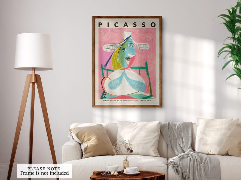 Modern abstract art featuring a striking figure with a large white hat, set against a vibrant pink background that evokes a sense of warmth and playfulness. The subject's face is characterized by angular shapes, bold outlines, and a mix of cool blues and greens, creating a dynamic contrast. The composition balances simplicity and complexity, with geometric elements and a whimsical expression. 'Femme 1938' by Picasso framed and displayed on a minimalist office wall. Printed poster wall art.
