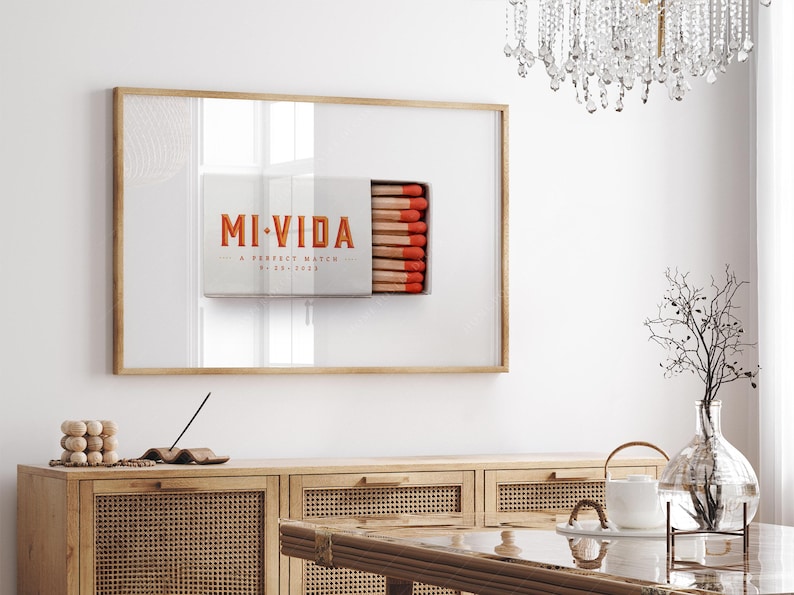 K&ouml;nnte beinhalten: Gerahmtes Kunstwerk mit einem Streichholzschachtel-Design, den Worten "MI VIDA" in Orange. Die Streichholzschachtel ist ge&ouml;ffnet und zeigt Streichh&ouml;lzer mit roten Spitzen. Das Kunstwerk h&auml;ngt &uuml;ber einem Holzschrank.