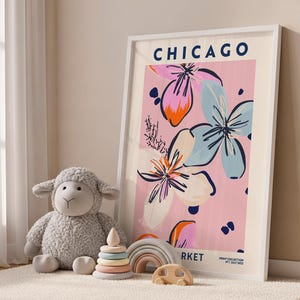 May include: A framed wall art print featuring the text CHICAGO and MARKET with a floral illustration in pink, blue, and orange. The print includes the text PRINT COLLECTION N&deg;1 JULY 2022. The artwork is displayed in a white frame.