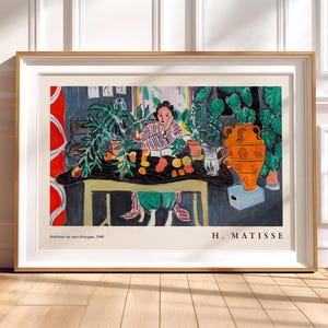 May include: A framed art print of Henri Matisse's 1940 painting Int&eacute;rieur au vase &eacute;trusque. The artwork depicts a person sitting at a table with fruit, plants, and an orange vase. The text H. MATISSE and the title are printed at the bottom.