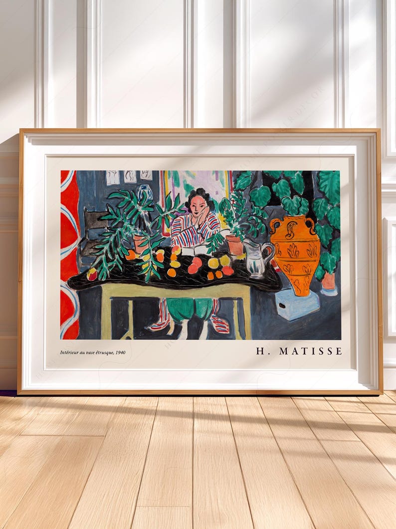 May include: A framed art print of Henri Matisse's 1940 painting Int&eacute;rieur au vase &eacute;trusque. The artwork depicts a person sitting at a table with fruit, plants, and an orange vase. The text H. MATISSE and the title are printed at the bottom.