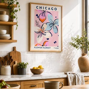 May include: A framed wall art print titled CHICAGO FLOWER MARKET featuring a pink background with stylized floral illustrations in shades of blue, white, and orange. The text CHICAGO appears at the top and FLOWER MARKET at the bottom in blue.