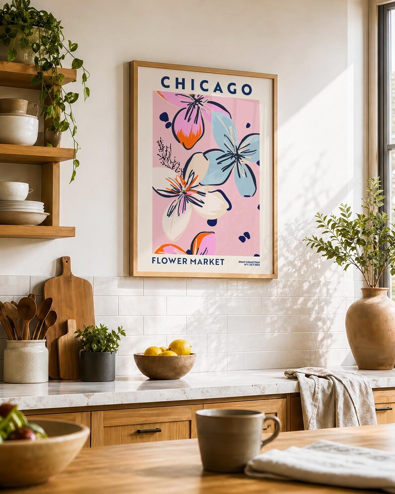 May include: A framed wall art print titled CHICAGO FLOWER MARKET featuring a pink background with stylized floral illustrations in shades of blue, white, and orange. The text CHICAGO appears at the top and FLOWER MARKET at the bottom in blue.