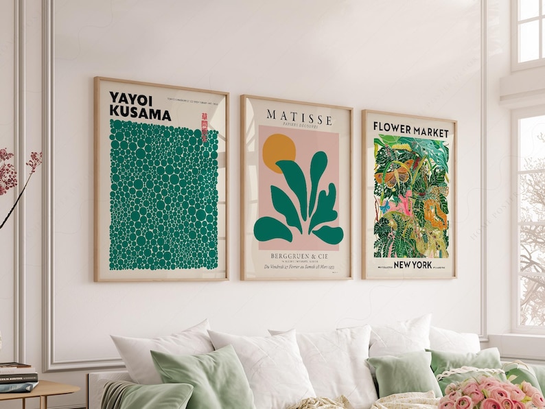 May include: Three framed art prints hanging on a wall. The left print features Yayoi Kusama text and a green dot pattern. The center print shows Matisse text, a yellow sun, and green leaves on a pink background. The right print displays Flower Market New York text with a colorful botanical illustration.