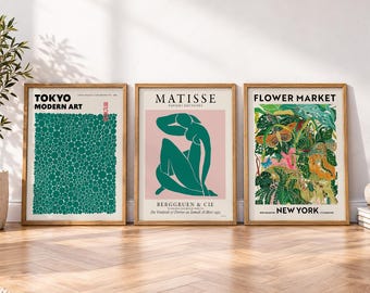 May include: Three framed wall art prints. The left print features green circles on a white background with text reading TOKYO MODERN ART. The center print shows a green abstract figure on a pink background with text MATISSE. The right print displays botanical illustrations with text FLOWER MARKET NEW YORK.