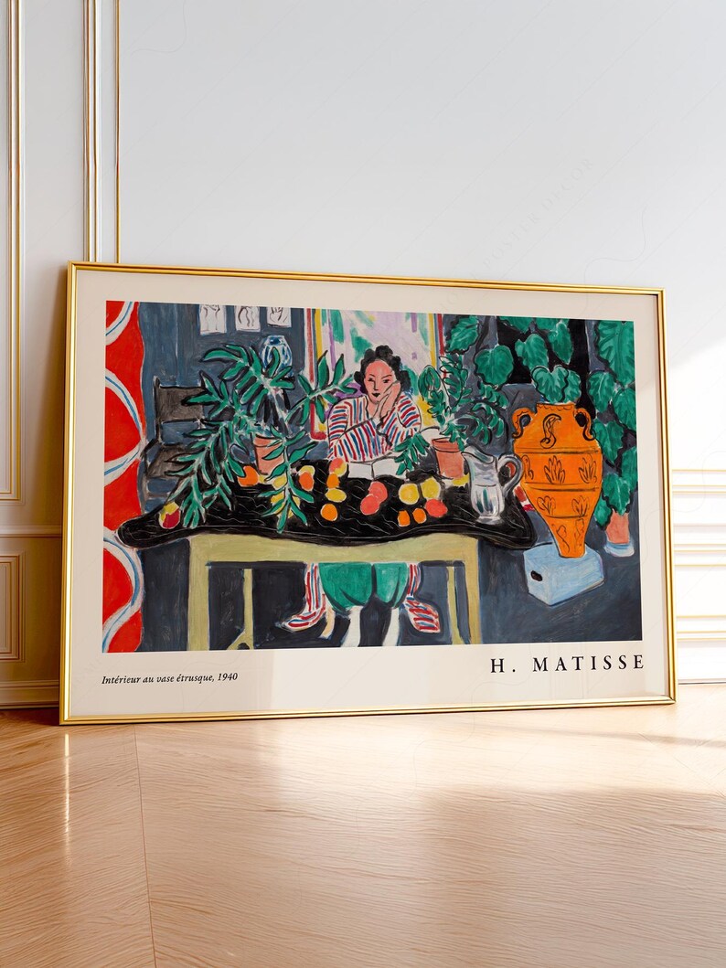 May include: A framed art print of Henri Matisse's 1940 painting Int&eacute;rieur au vase &eacute;trusque, featuring a person at a table with fruit, plants, and an orange vase. The print has a gold frame and includes the artist's name and the title at the bottom.