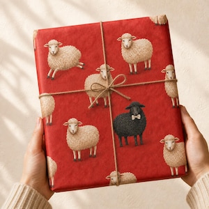 May include: A rectangular gift wrapped in vibrant red paper featuring a repeating pattern of fluffy beige sheep and one singular black sheep wearing a small beige bow tie. The package is tied with a thin, natural brown jute twine string.