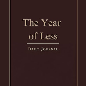 Op de afbeelding: Een donkerbruin dagboek met een witte rand en de tekst "The Year of Less" en "Daily Journal" in een lichtbruine letter.