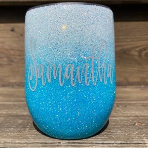 May include: A blue and white ombre glitter tumbler with the name "Samantha" written in white on the side.