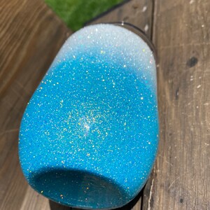 May include: A blue and white ombre glitter tumbler with a stainless steel lid. The tumbler is made of a durable material and is perfect for keeping drinks cold or hot.
