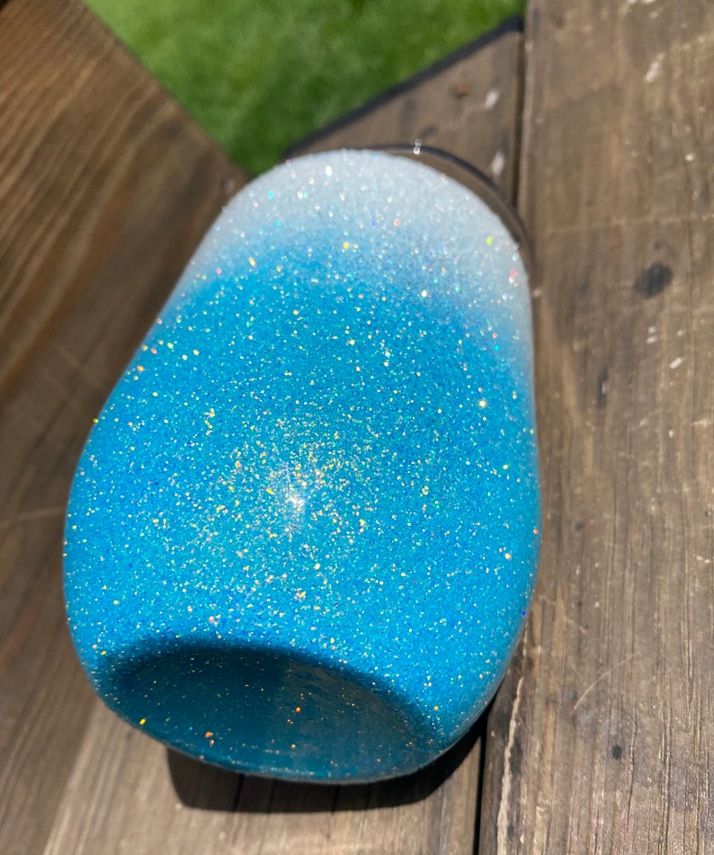 May include: A blue and white ombre glitter tumbler with a stainless steel lid. The tumbler is made of a durable material and is perfect for keeping drinks cold or hot.
