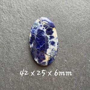 May include: A blue and white oval cabochon gemstone with a marbled pattern. The stone measures 42 x 25 x 6 mm.